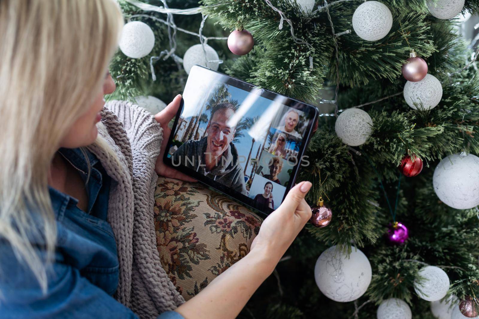 Woman with santa hat using video call conference on tablet, decorations and lights at home. Caucasian adult for christmas eve party.