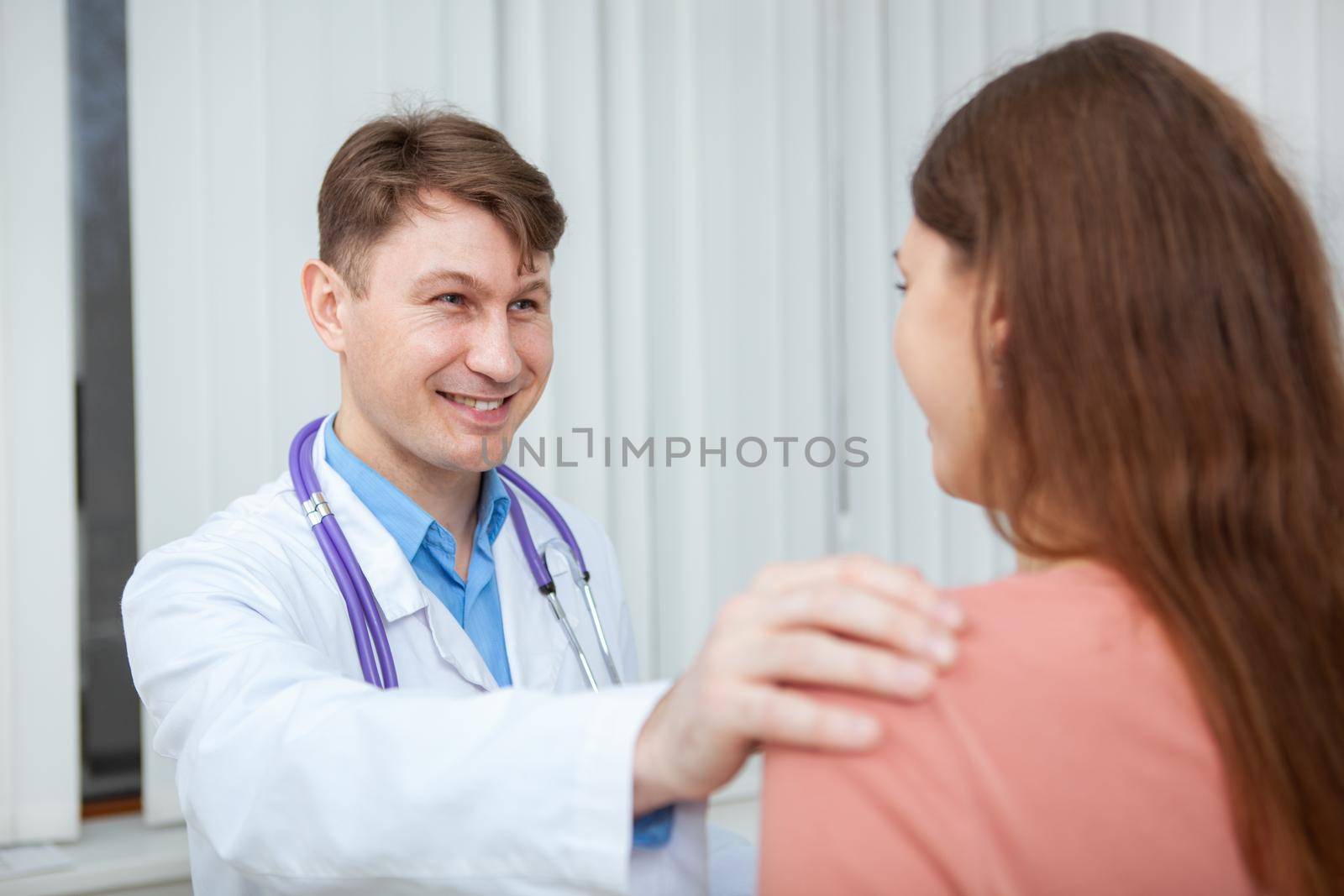 Cheerful male doctor smiling, comforting his female patient. Mature male practitioner cheering up young woman, helping her get healthier