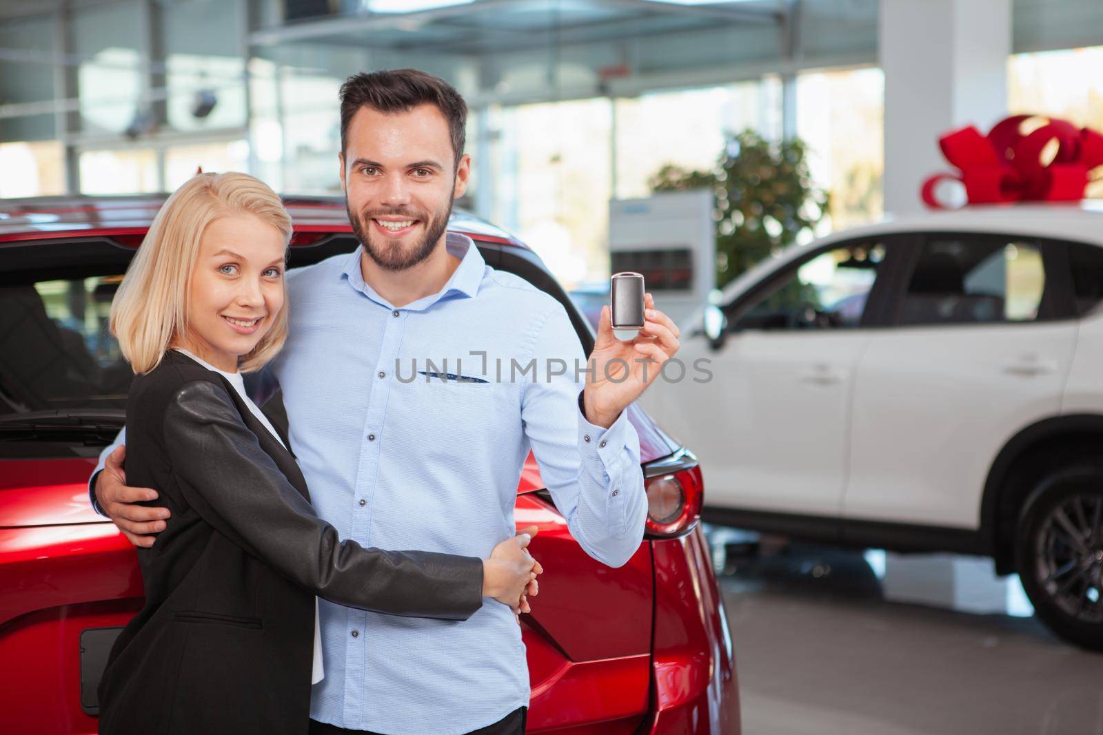 Handsome happy man hugging his lovely wife smiling to the camera with a car key in his hand, copy space. Couple celebrating buying new auto