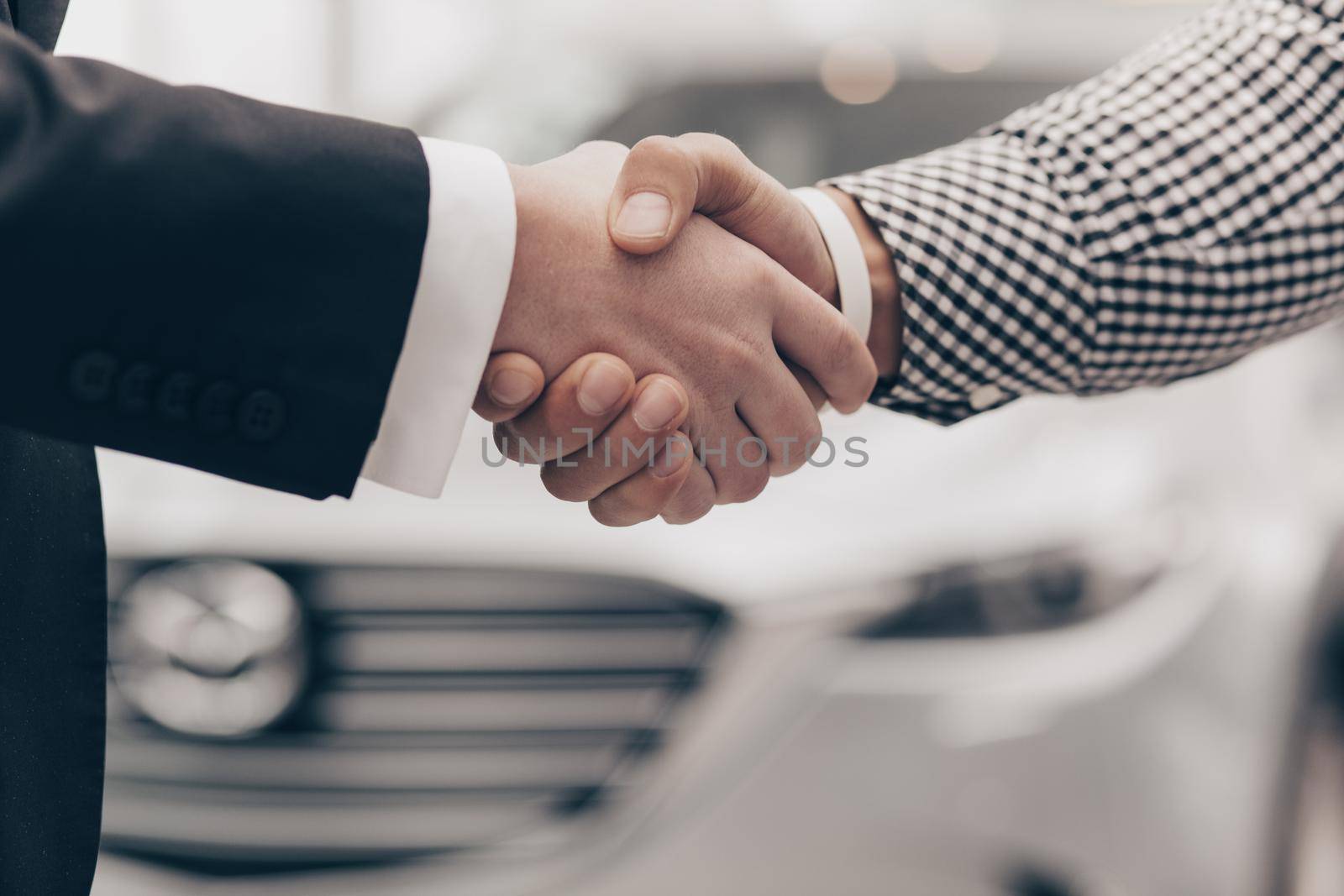 Cropped close up of a handshake of two men at the dealership salon. Salesman shaking hands with his customer after closing the deal on car for sale. Man buying new automobile. Ownership concept