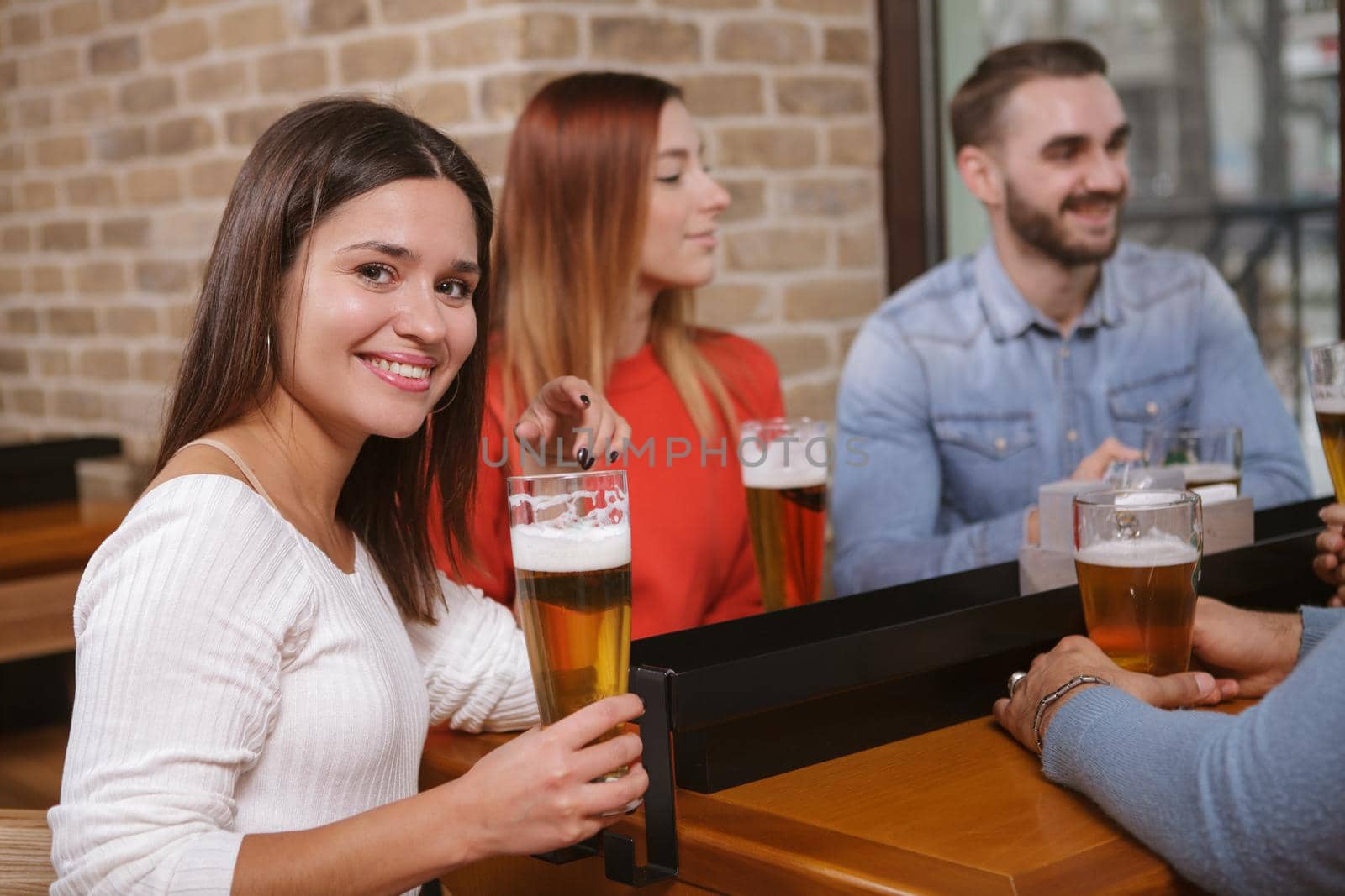 Cheerful woman smiling to the camera while drinking beer with her friends at local pub