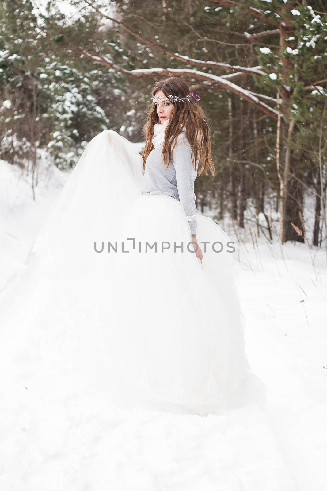 Beautiful bride in a white dress with a bouquet in a snow-covered winter forest. Portrait of the bride in nature.