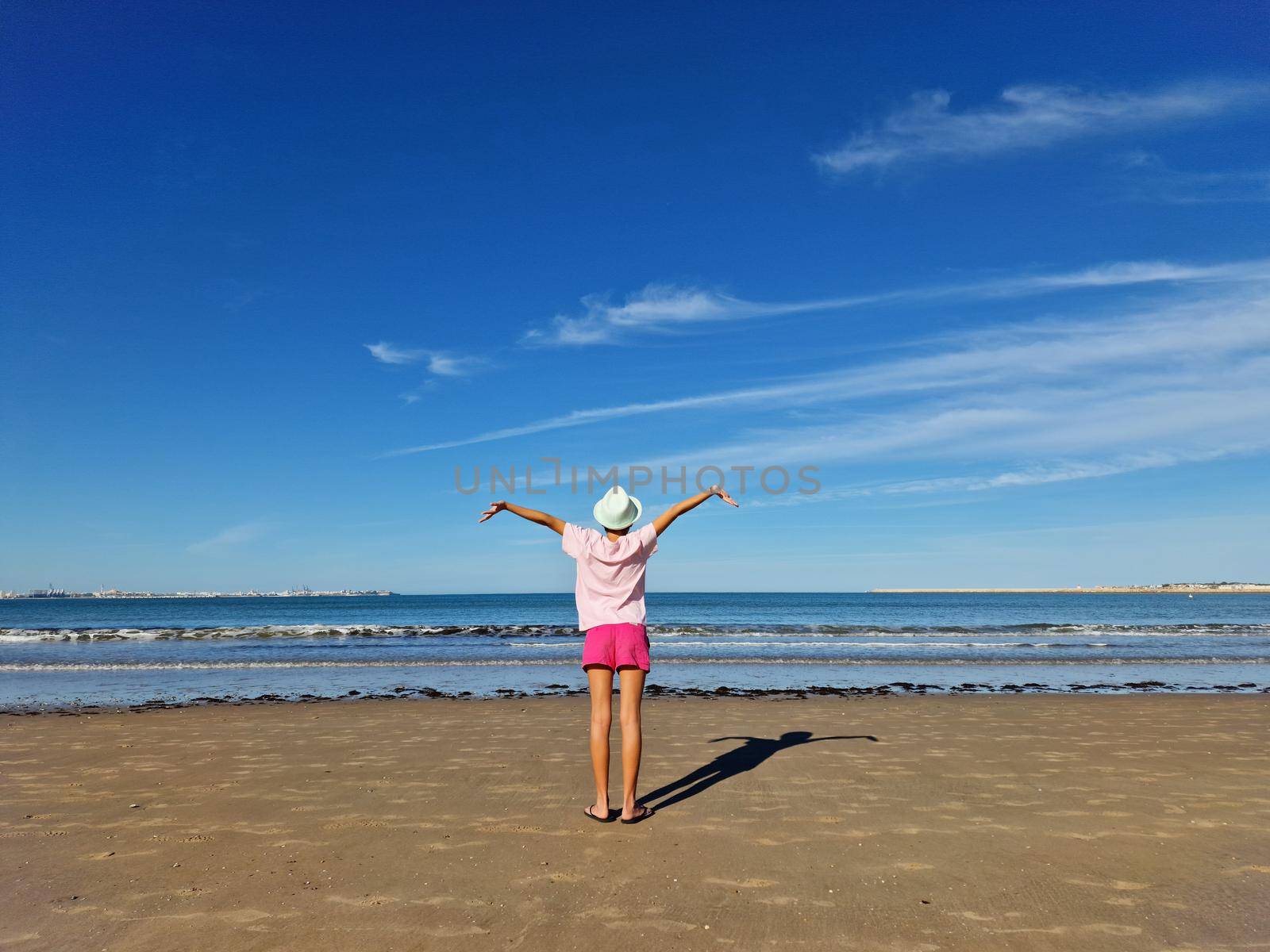 Girl with hat opening her arms in front of the sea, on a sandy beach. by javiindy