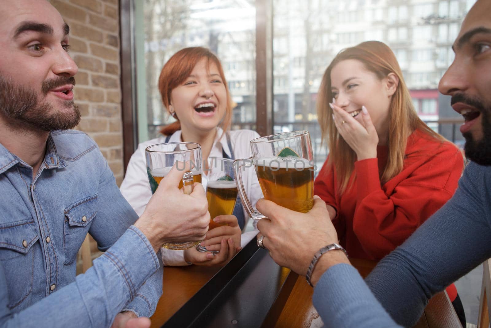 Cheerful friends laughing and talking over a glass of beer at local pub. Friendship, youth concept