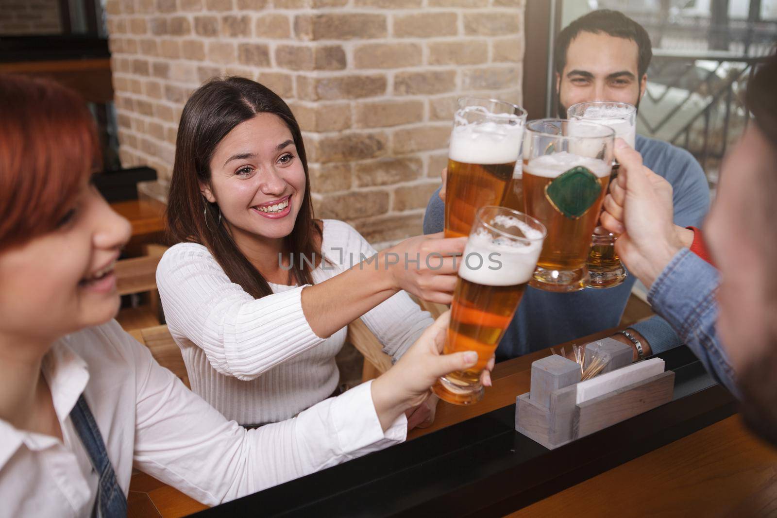 Group of friends clinking their beer glasses, celebrating together at the pub