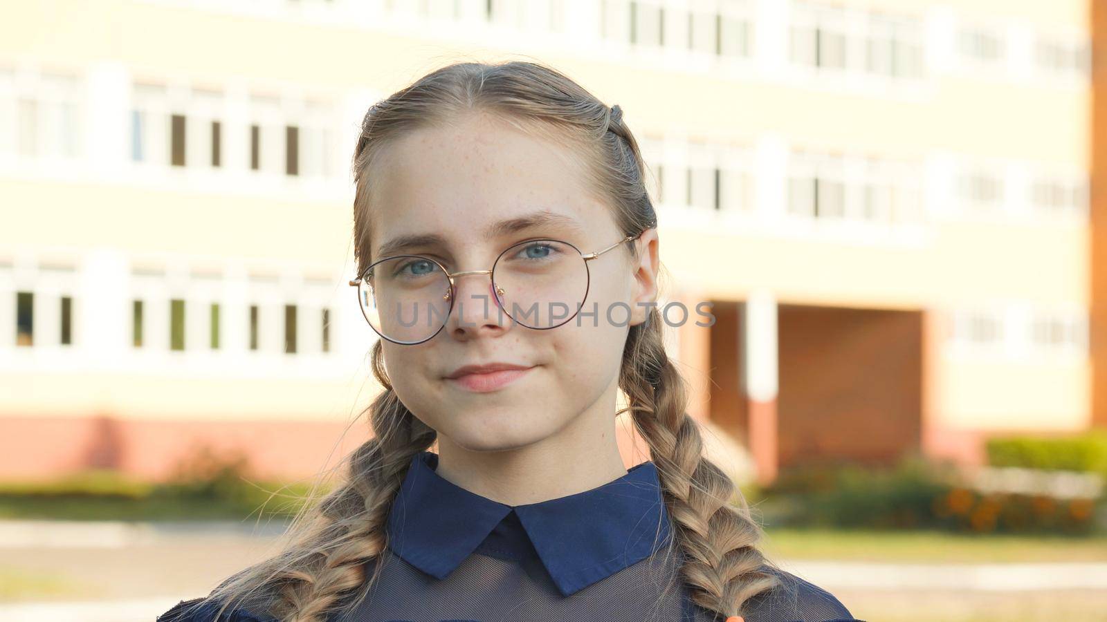 A teenage girl wearing glasses in front of a school