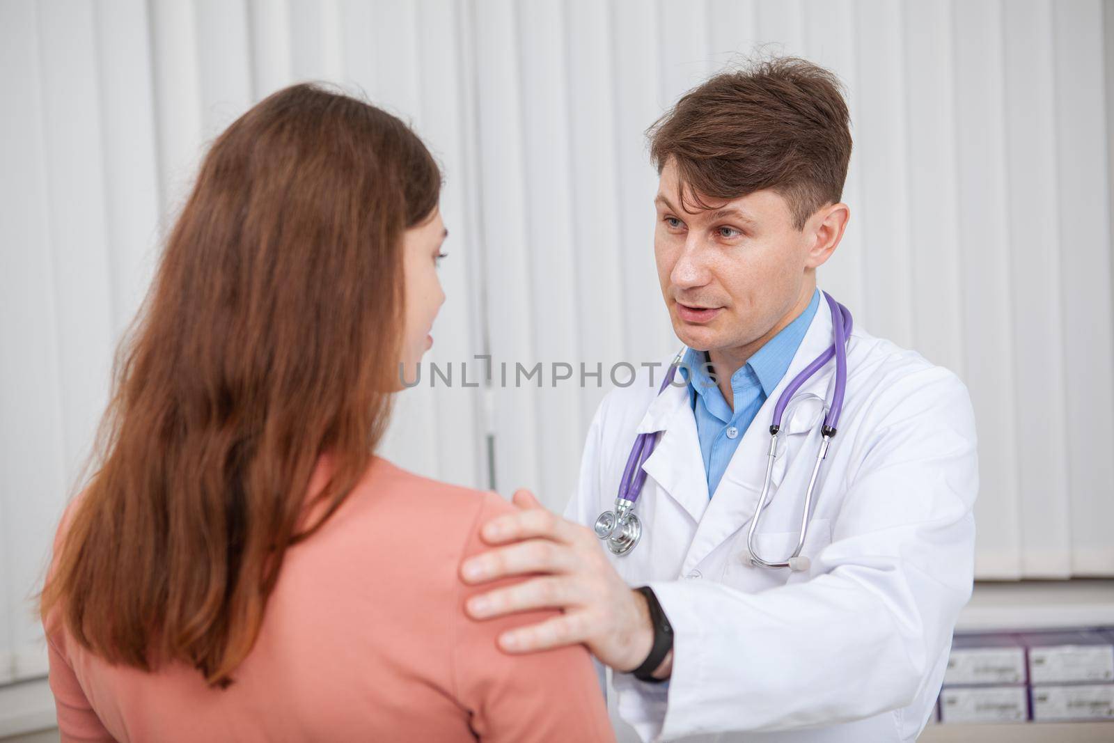 Mature male doctor working at his clinic, talking to a female patient. Experienced doctor comforting his upset patient