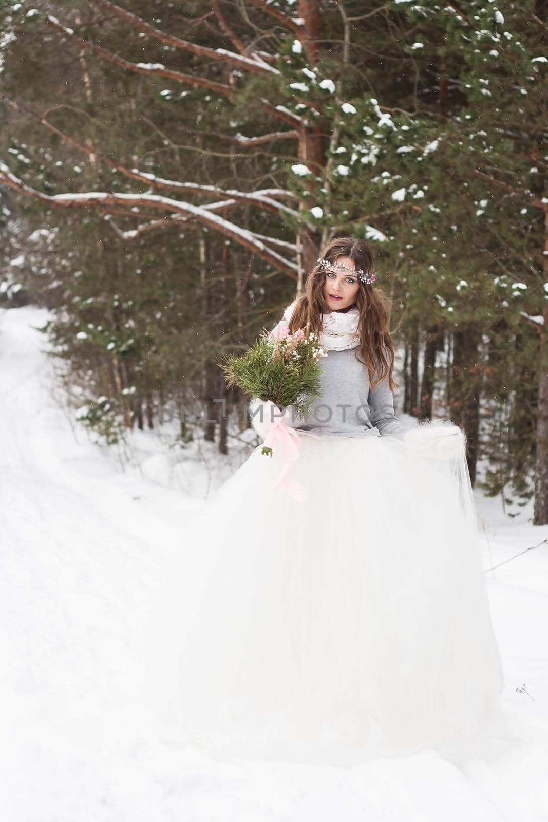 Beautiful bride in a white dress with a bouquet in a snow-covered winter forest. Portrait of the bride in nature.