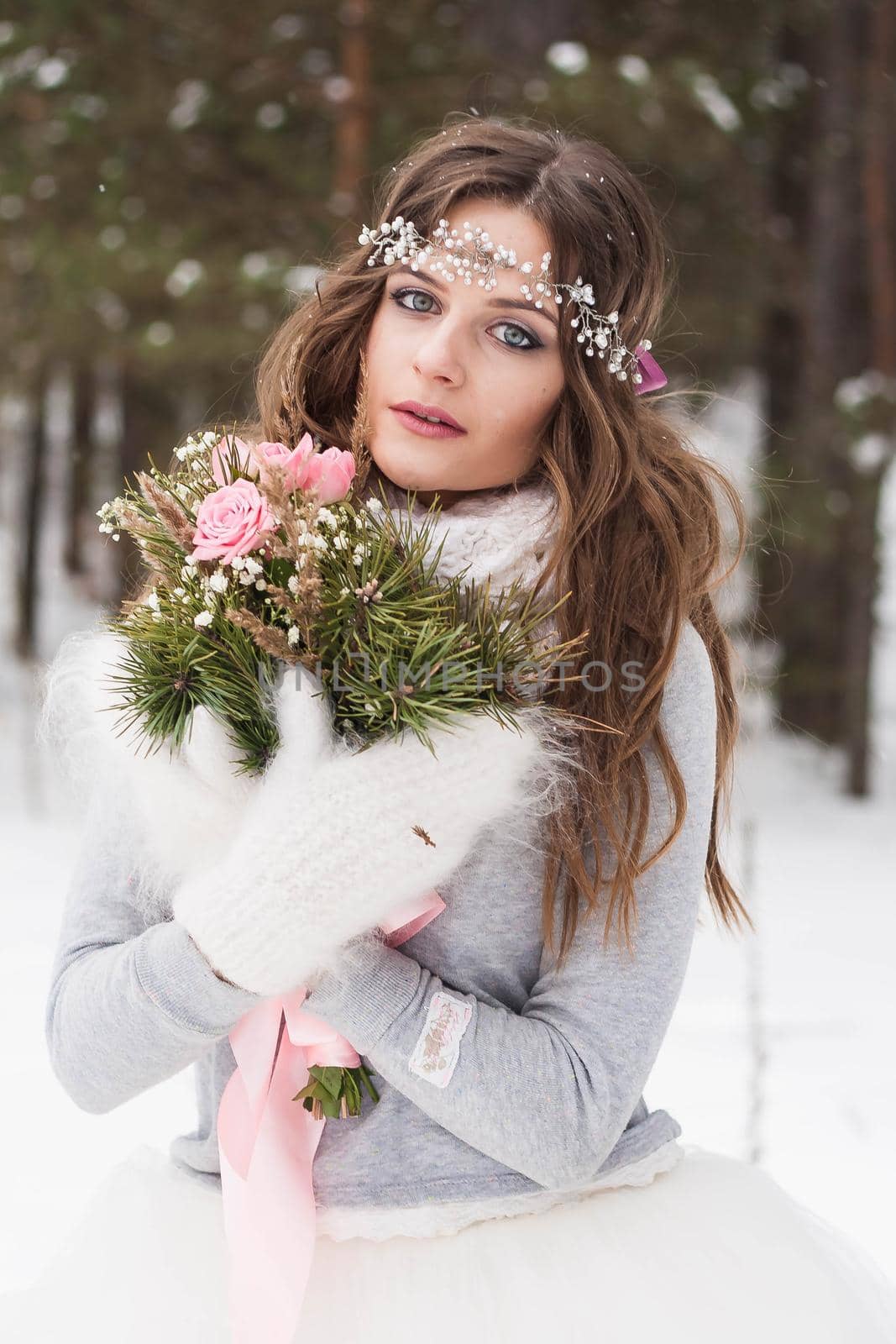 Beautiful bride in a white dress with a bouquet in a snow-covered winter forest. Portrait of the bride in nature.