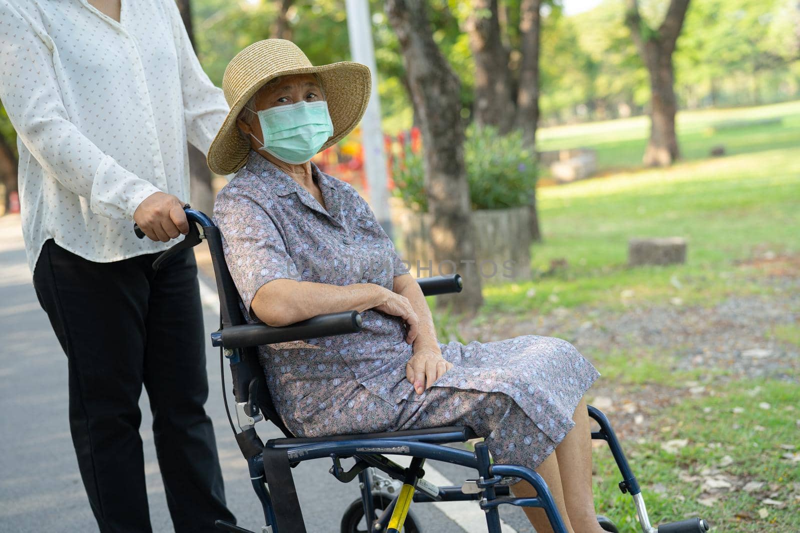 Help Asian senior or elderly old lady woman on wheelchair and wearing a face mask for protect safety infection Covid19 Coronavirus in park. by pamai
