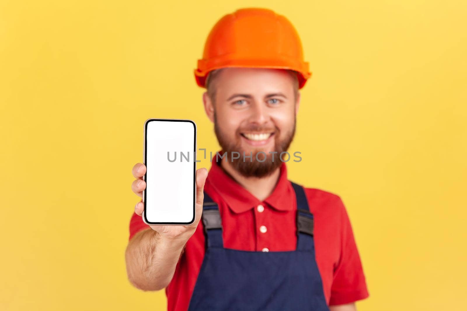 Builder man in uniform and protective helmet holding smart phone with blank screen for advertisement by Khosro1