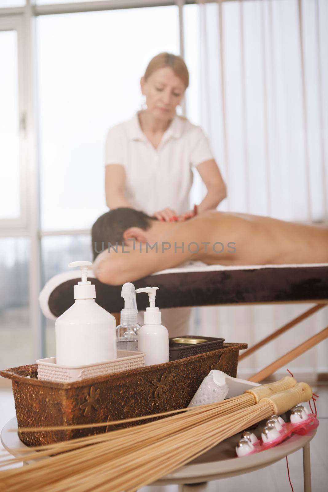 Selective focus on massage oil bottles and body massage tools, professional masseur working on background