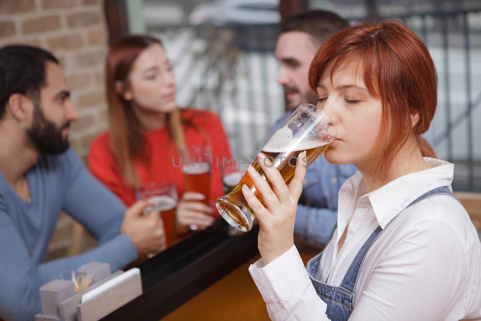 Close up of a young woman enjoying drinking delicious beer with her friends. Woman sipping craft beer at the pub