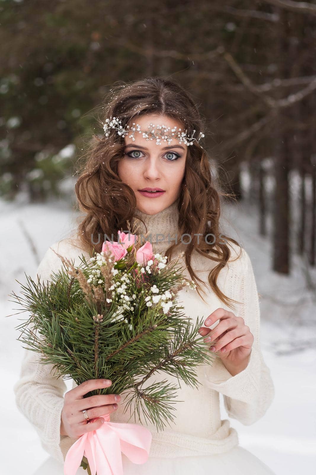 Beautiful bride in a white dress with a bouquet in a snow-covered winter forest. Portrait of the bride in nature.