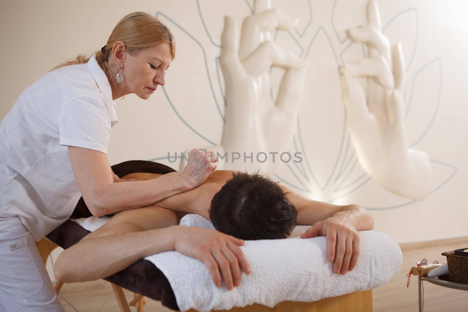 Senior professional masseur working at spa center, massaging back of a man, copy space