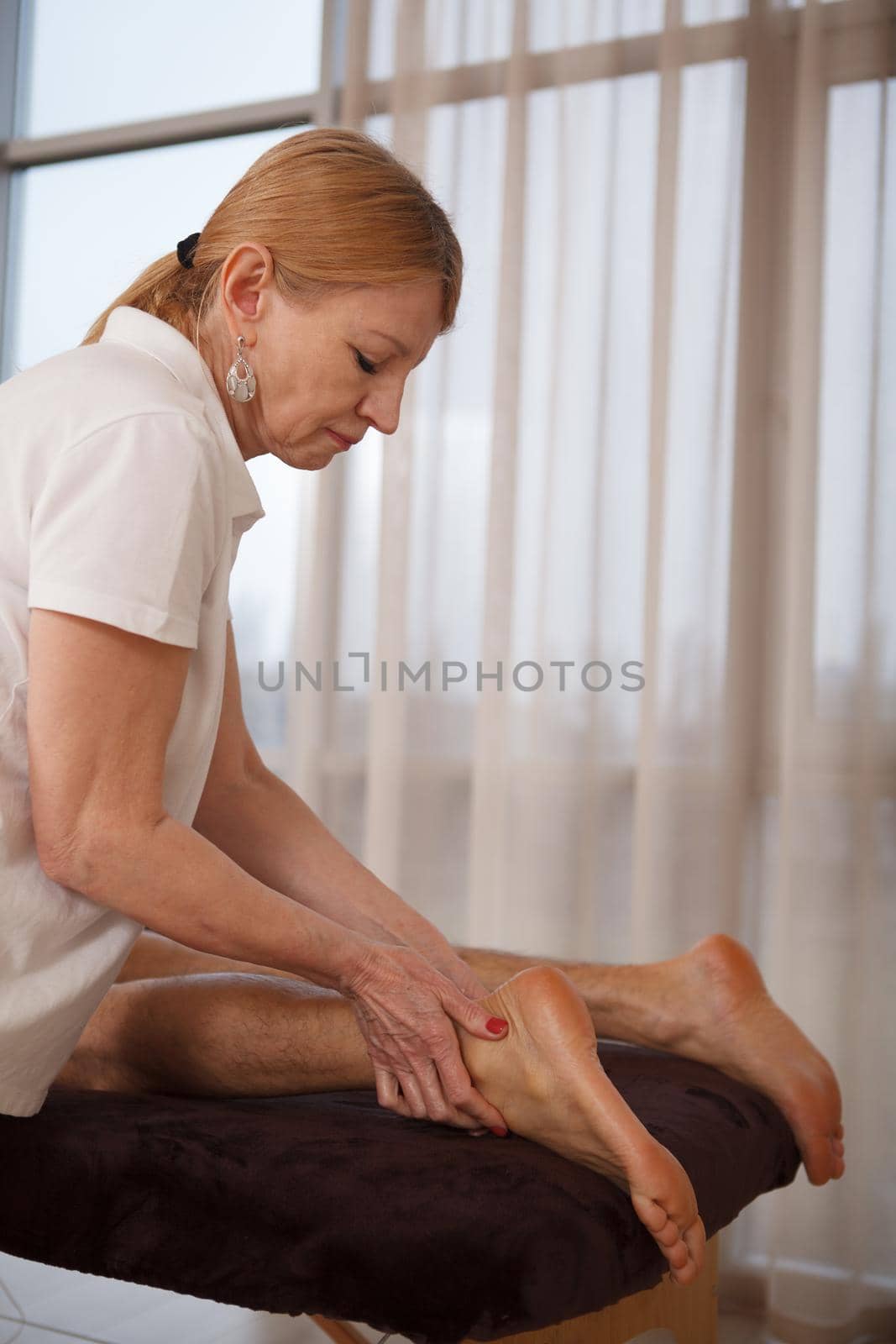 Vertical shot of a senior female masseur working at spa center, doing foot massage for a client