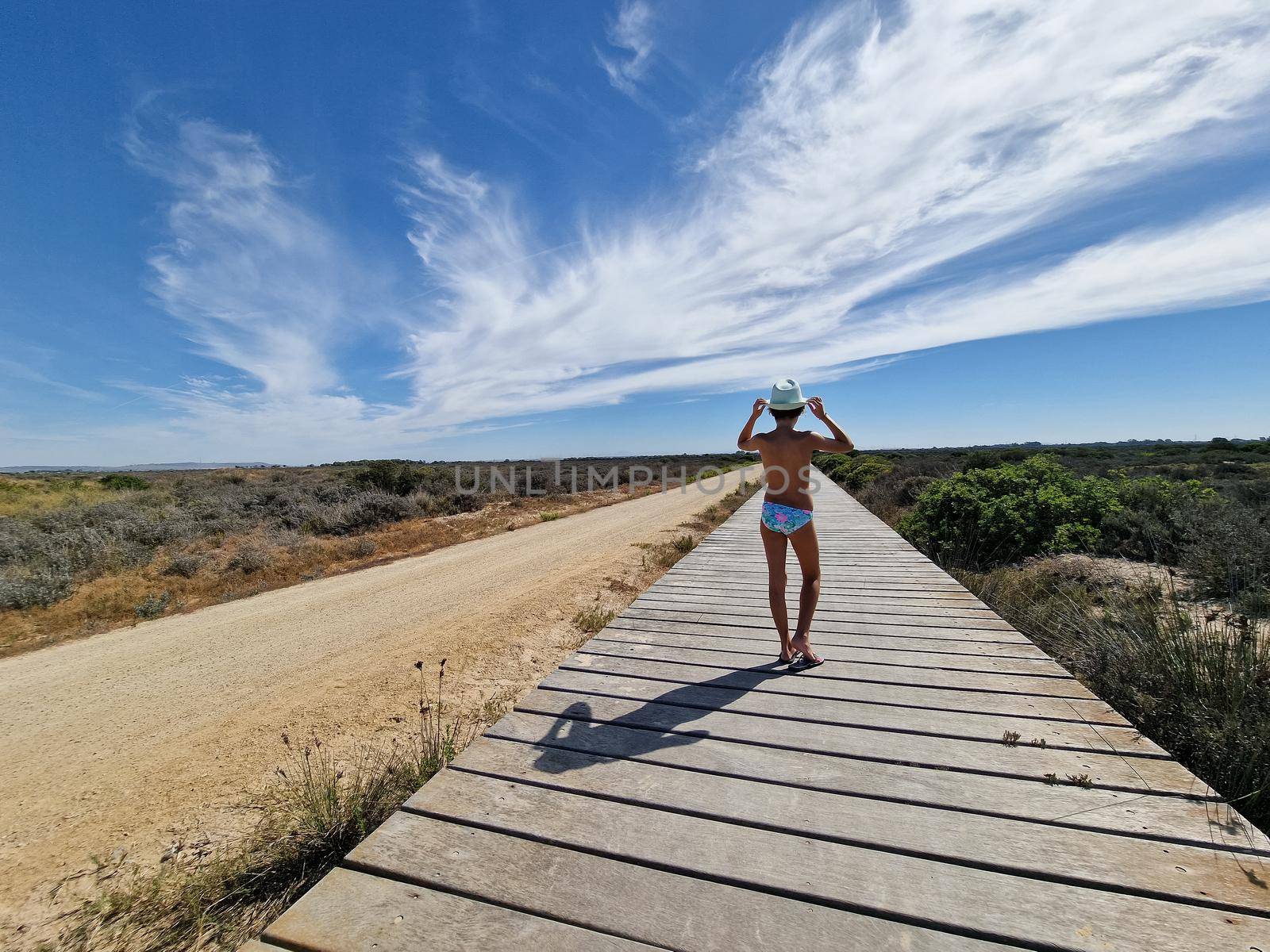 Girl on a path of wooden planks on the sand near Valdelagrana beach, with beautiful clouds in the sky. Puerto de Santa Maria, Cadiz, Andalusia, Spain.
