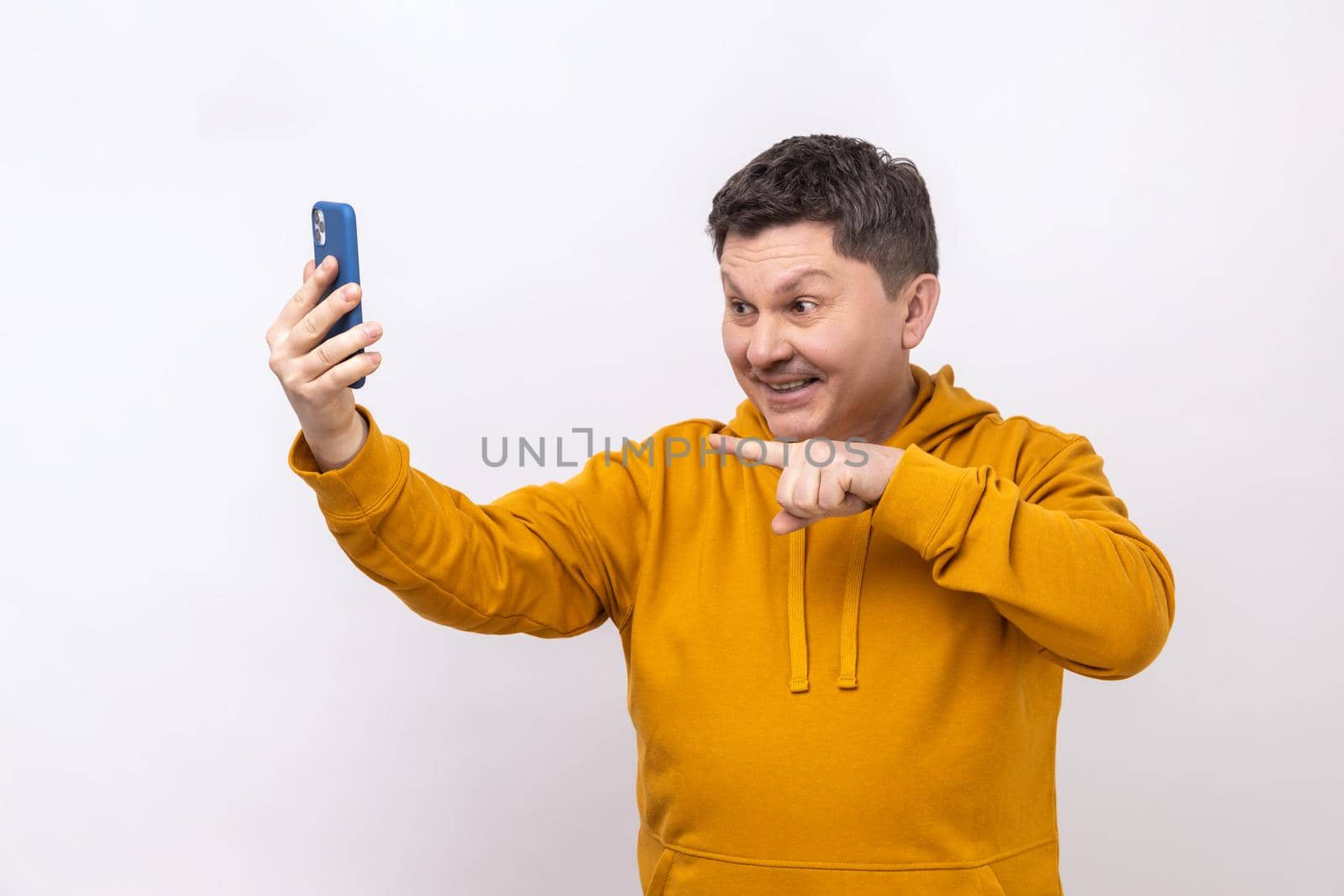 Portrait of smiling middle aged man pointing to cell phone camera while having video call or livestream, wearing urban style hoodie. Indoor studio shot isolated on white background.