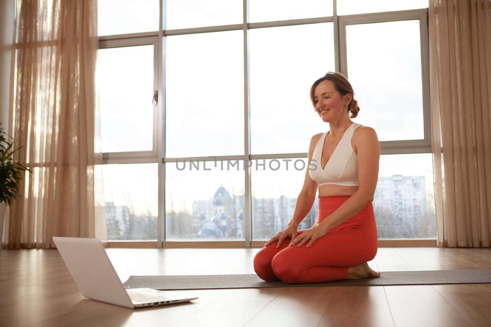 Middle aged woman teaching online yoga class, using her laptop