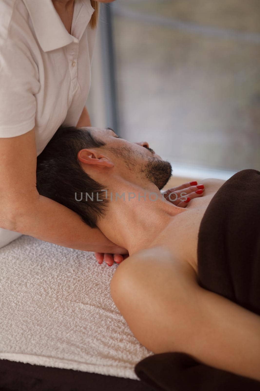 Vertical cropped shot of a man enjoying professional neck and shoulders massage at spa salon