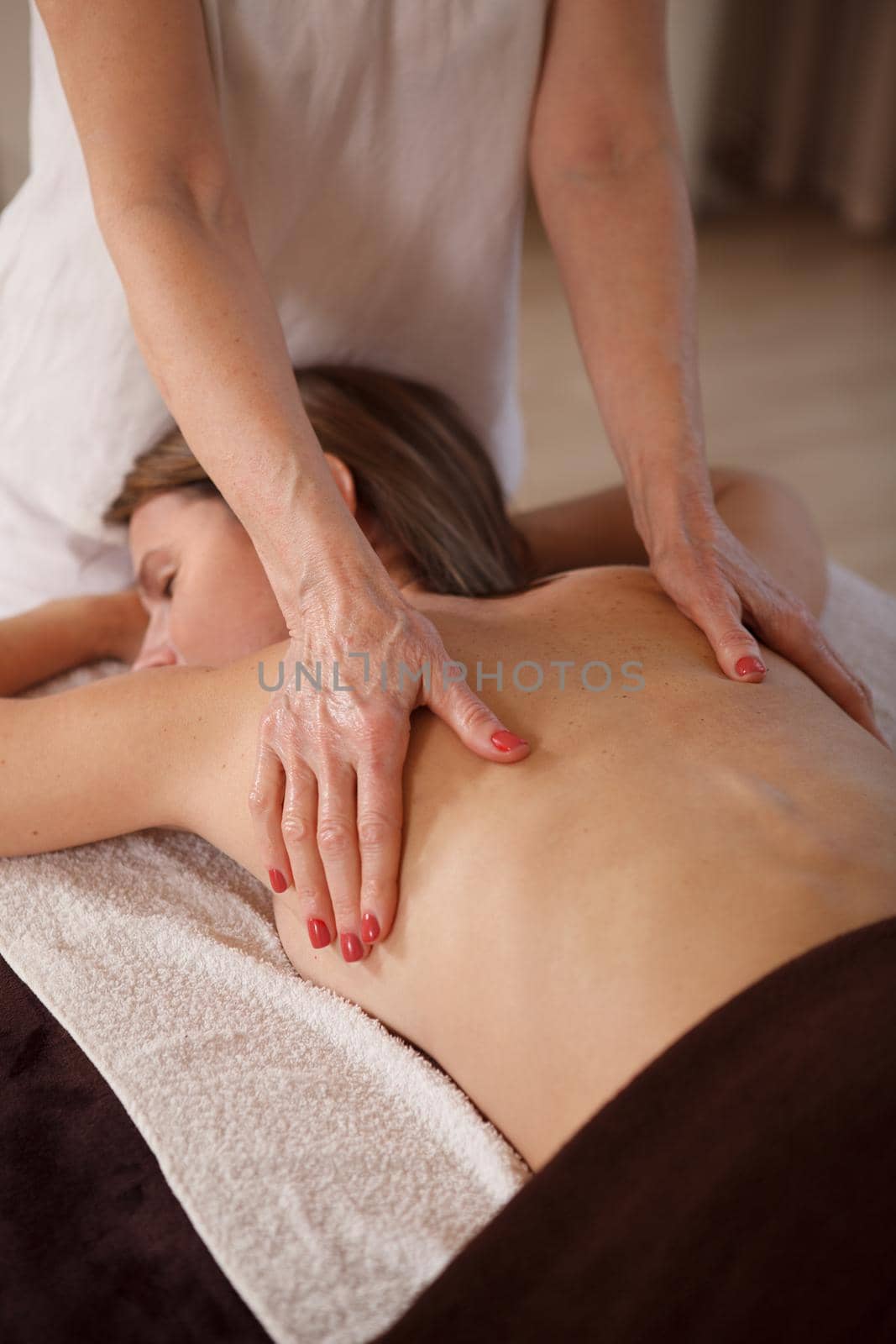 Vertical shot of a woman relaxing at spa center, getting back massage