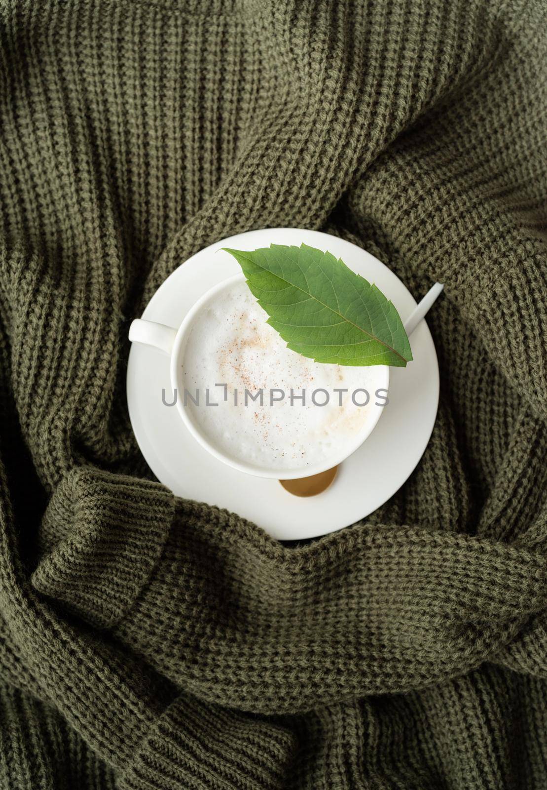 cup of cappuccino coffee on green sweater top view flat lay by Desperada