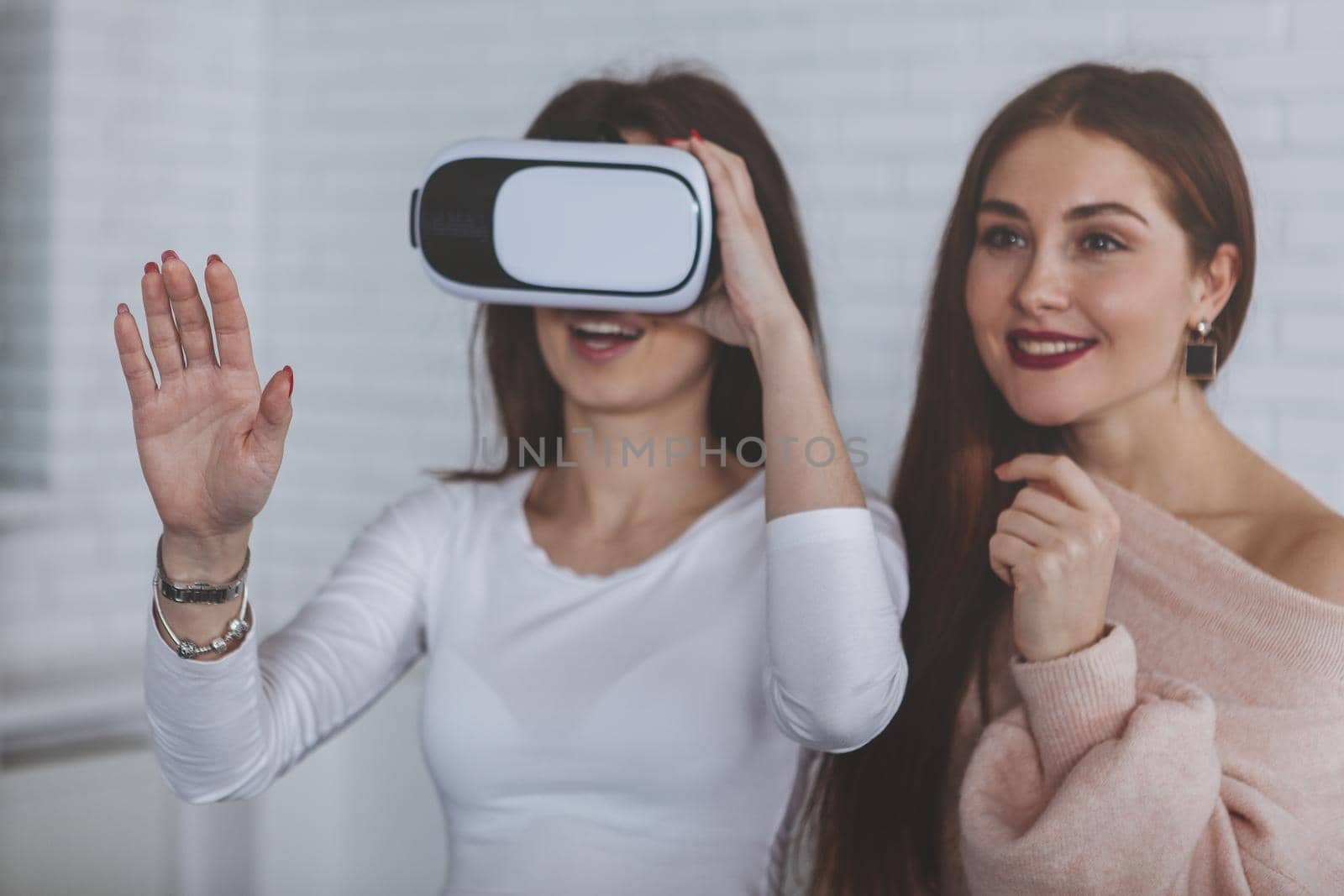 Two young women enjoying using virtual reality glasses together. Beautiful woman looking excited, her friend wearing 3d vr headset, copy space. Startup, modern technology, development concept