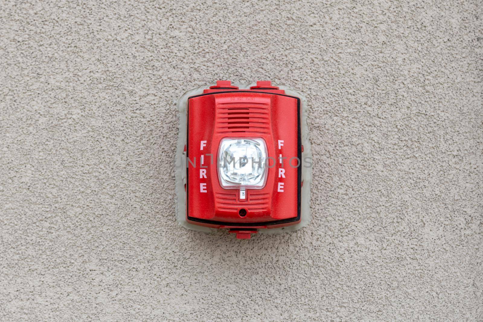 Red fire alarm siren with flashing light strobe isolated on gray cement wall outdoor. Fire safety. by Khosro1