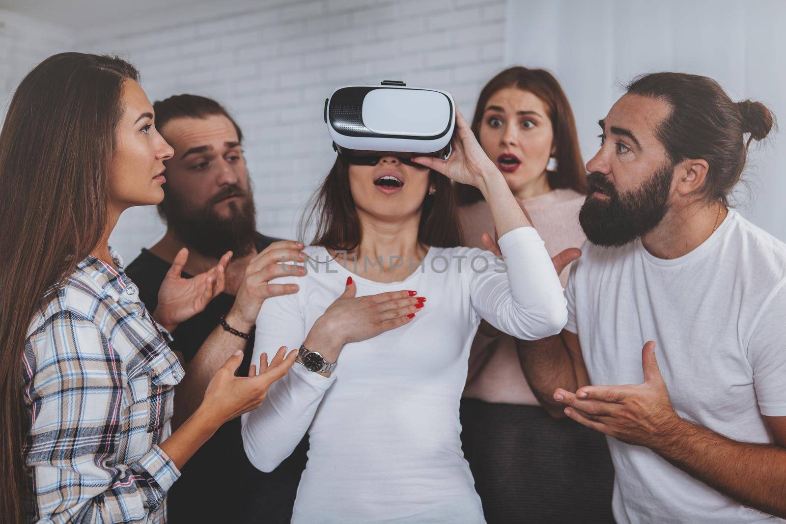 Young woman looking overwhelmed and shocked, wearing virtual reality headset, her friends surrounding her. Group of businesspeople working together on innovative project, using vr goggles