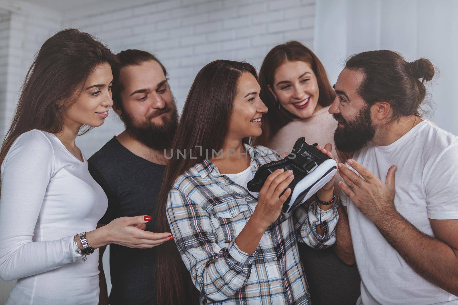 Charming young woman talking to her colleagues joyfully, holding virtual reality glasses. Group of coworkers discussing experience of using 3d vr goggles. Digital, technology concept