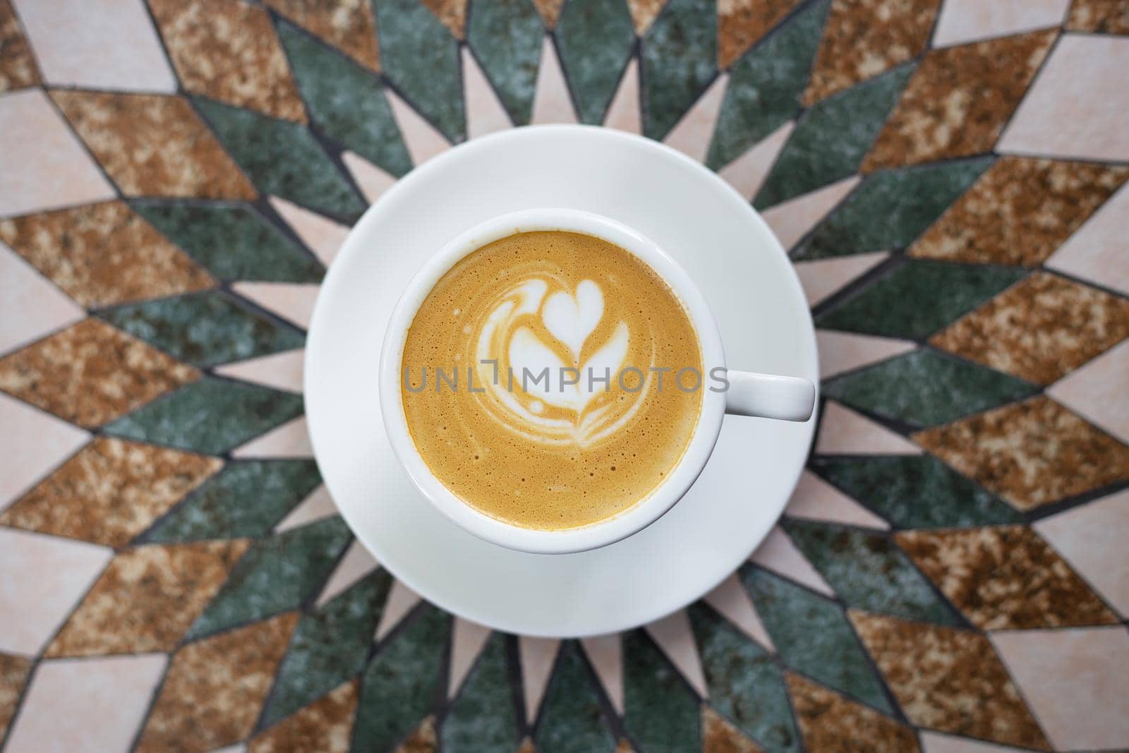 White cup of cappuccino coffee with heart-shaped foam on a beautiful table. View from above