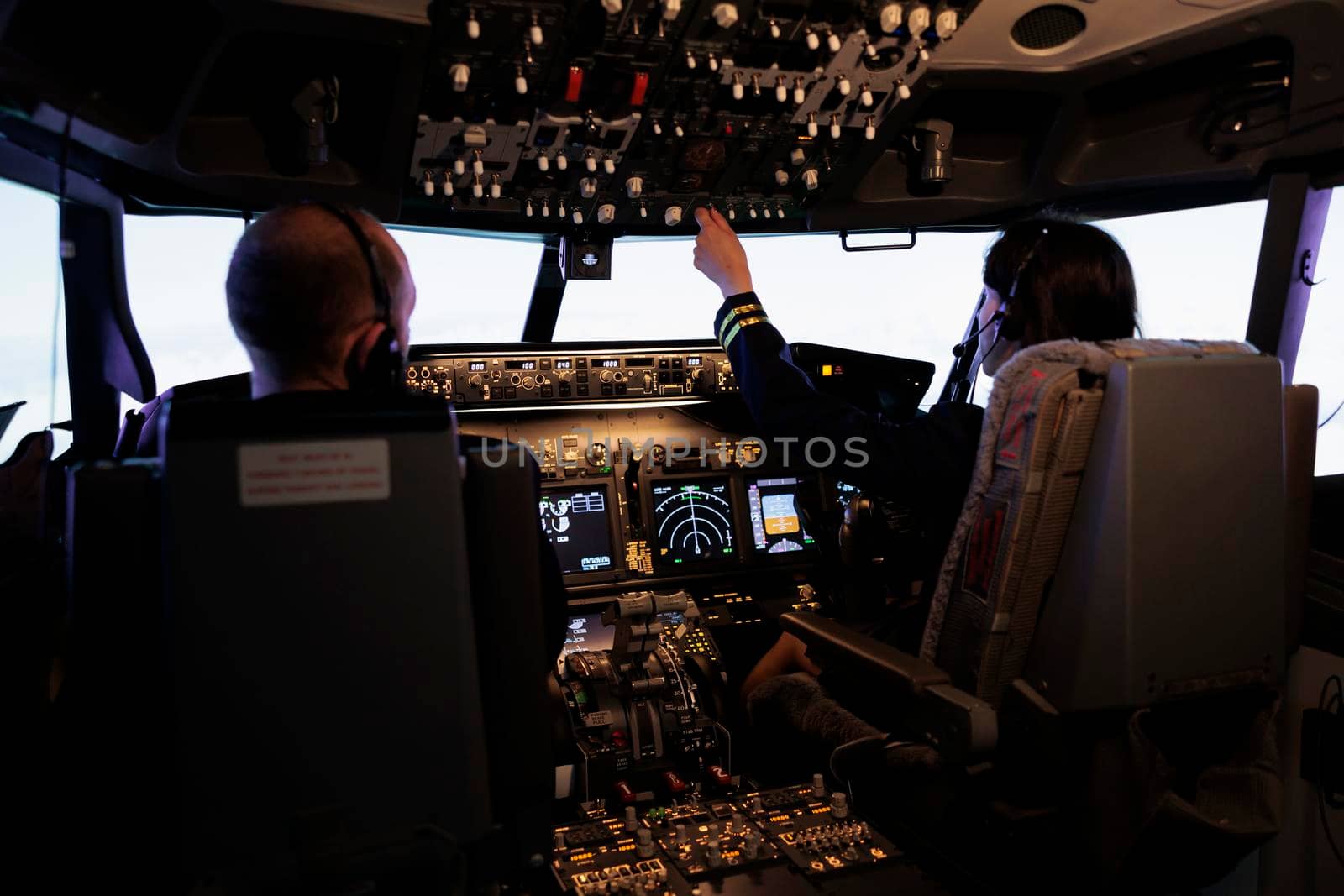 Woman copilot assisting captain to takeoff and fly airplane, using buttons on dashboard command in pilot cockpit. Airliners flying plane jet with navigation windscreen and control panel.