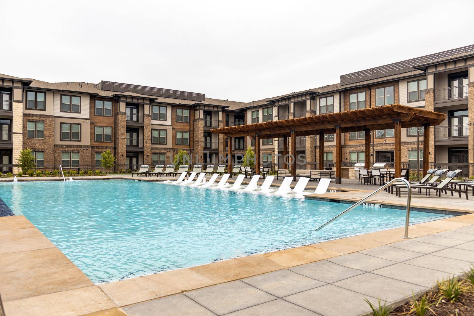 Empty white deck chairs near the swimming pool and modern building, resting area in the hotel