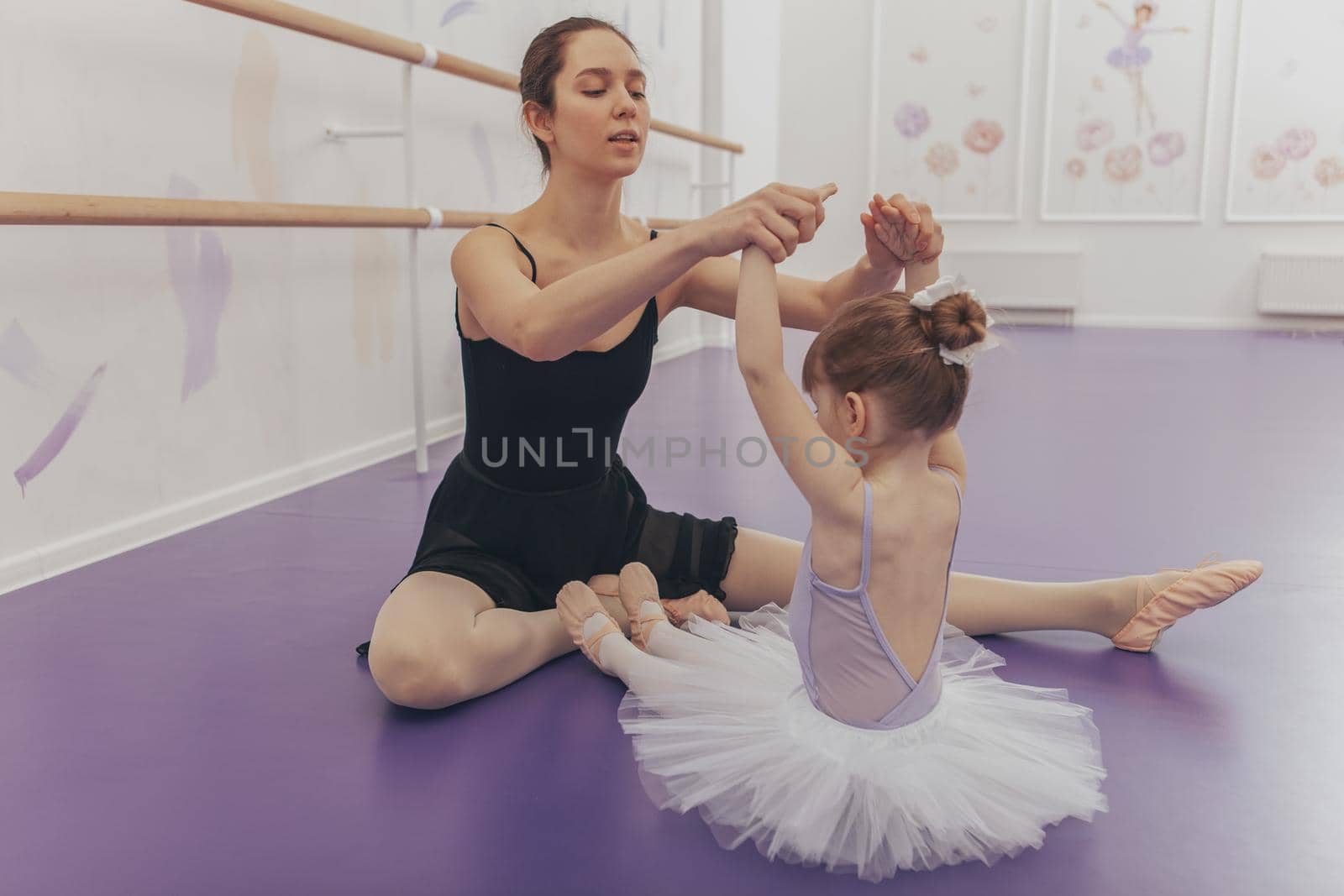 Adorable little ballerina exercising with her ballet teacher at dance school. Beautiful young woman ballet dancer teaching her little student. Education, experience, achievement concept