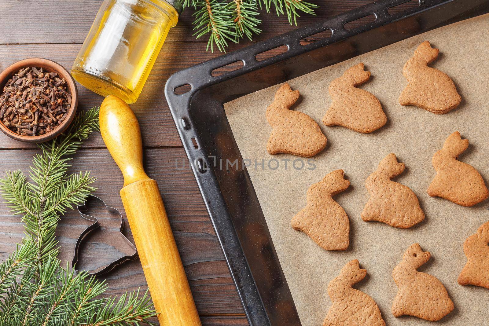 Ready-made Christmas cookies in the form of a rabbit on a baking sheet on a wooden table decorated with Christmas tree branches, with a jar of honey and cloves. Symbol of 2023 by lara29