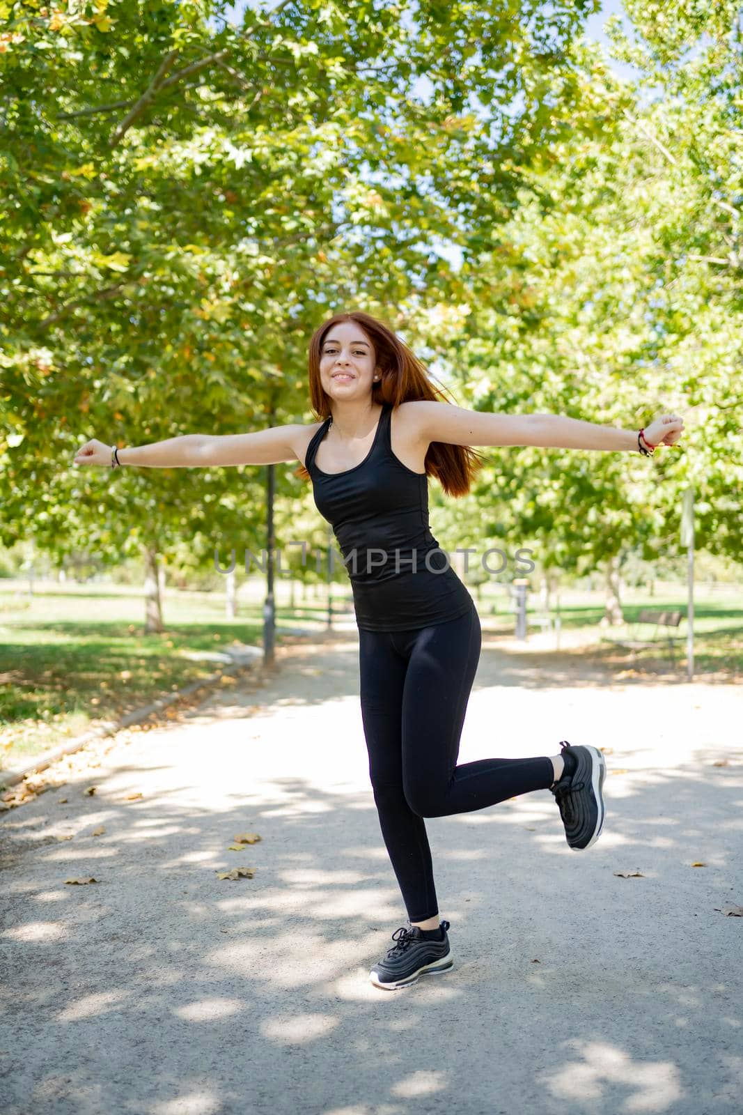 Sporty redheaded young woman dancing on the green grass of a public park. stock photography