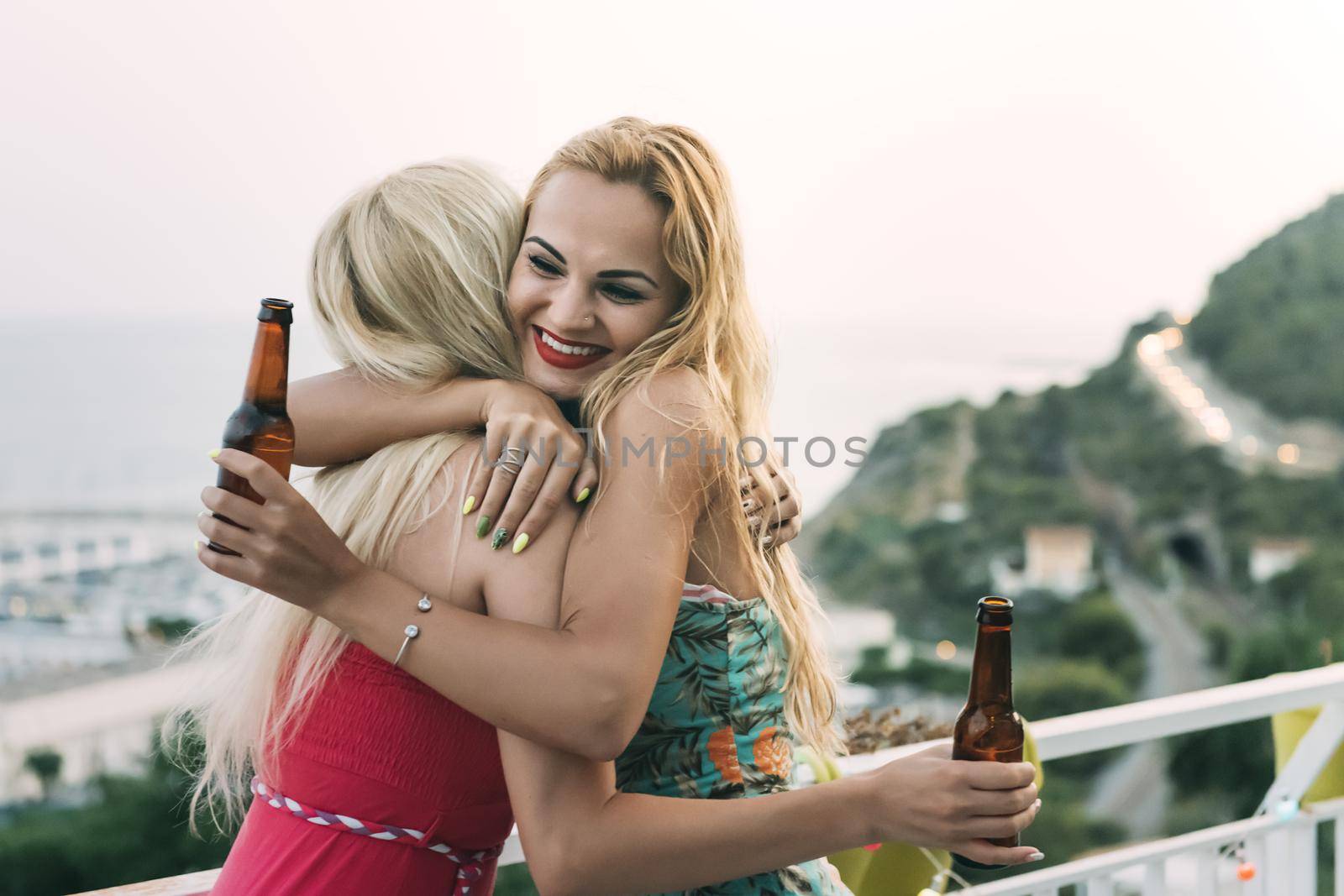 carefree young girls with beers hugging and having fun at a private party on the outdoor terrace, leisure happiness and friendship concept, with copy space for text