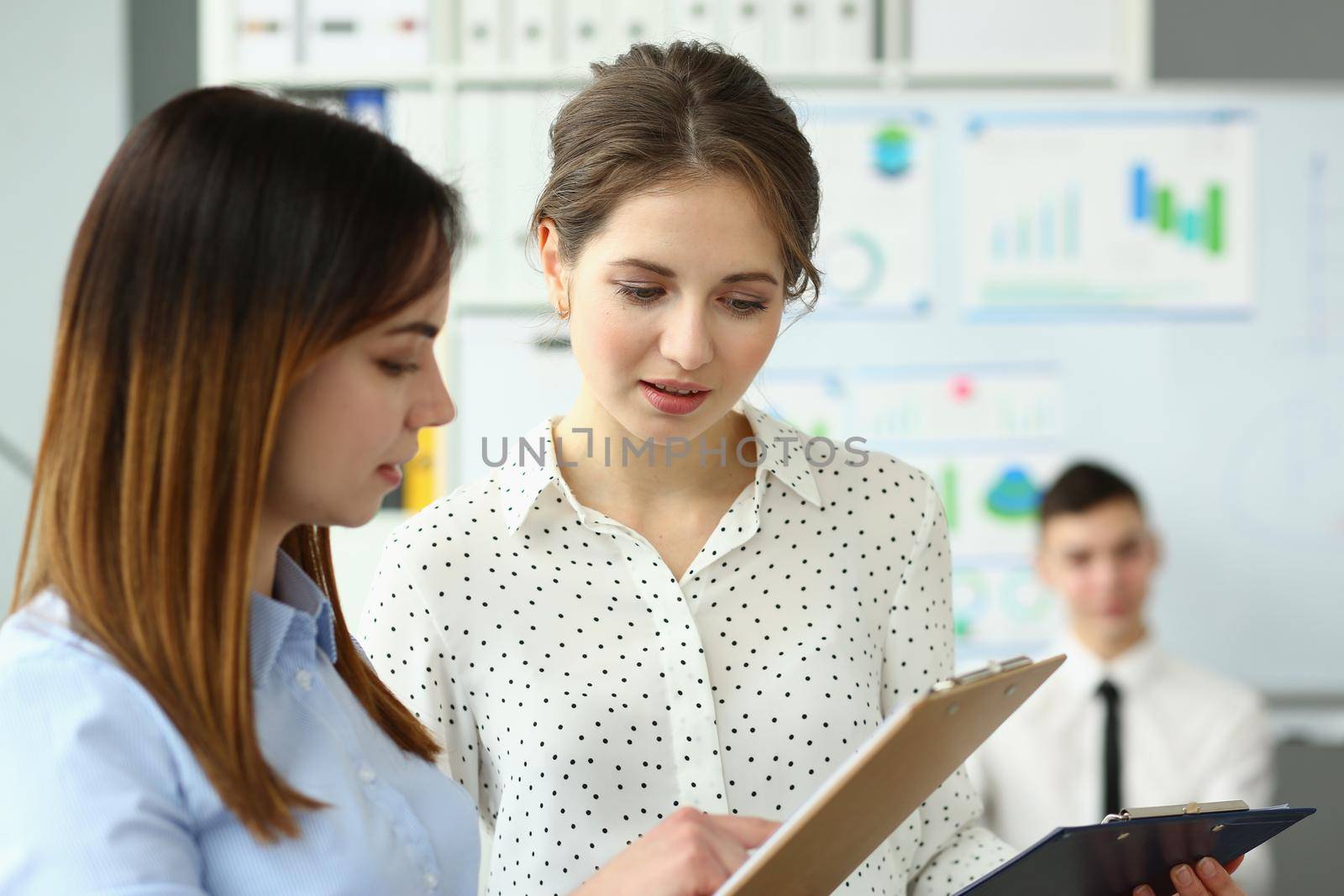Two beautiful businesswoman discussing business document standing in office by kuprevich