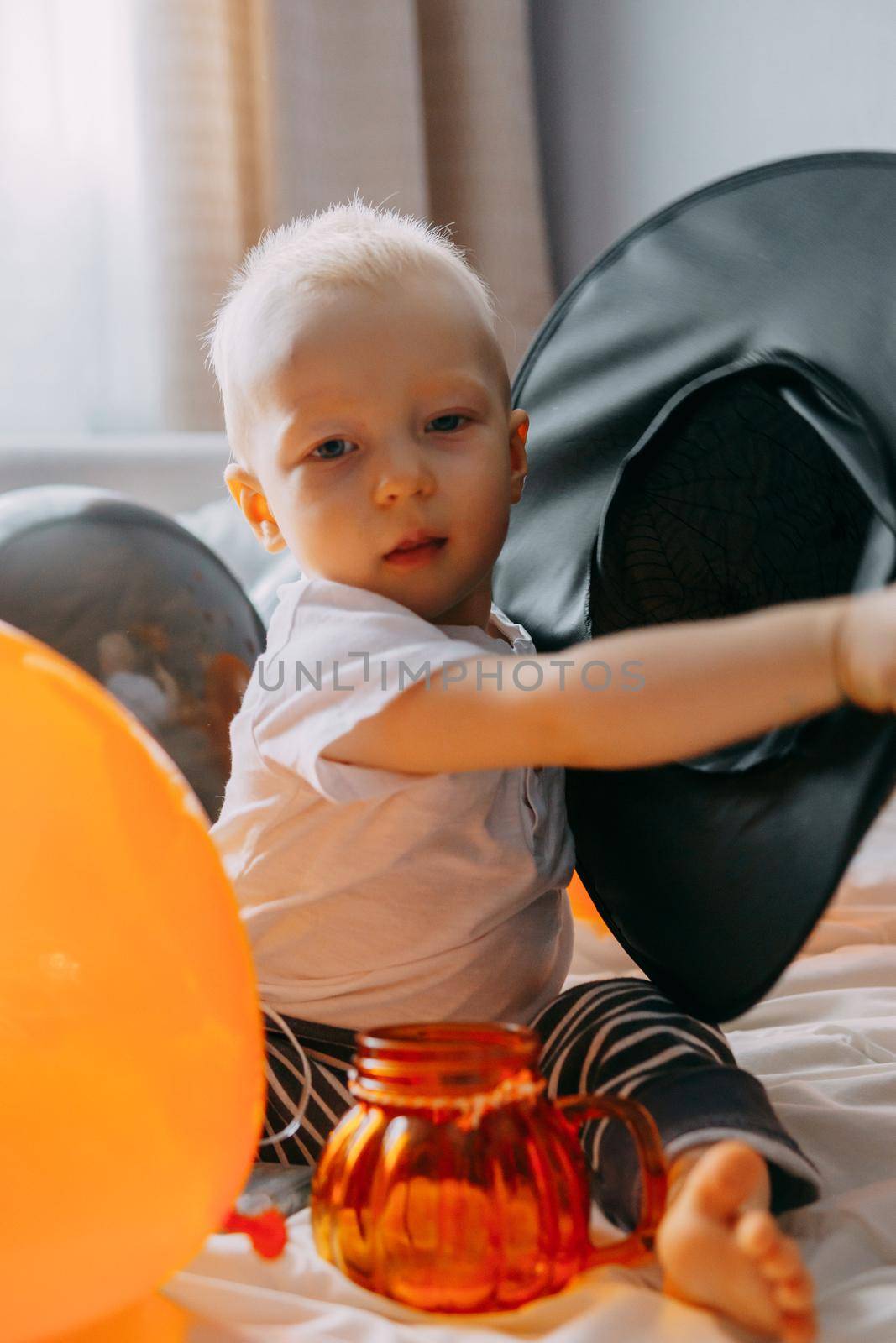 Children's Halloween - a boy in a witch hat and a carnival costume with airy orange and black balloons at home. Ready to celebrate Halloween.