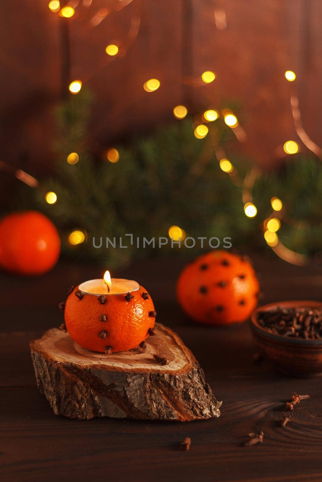 A tangerine candlestick on a wooden stand on a table decorated with fir branches and Christmas lights. Handmade.copy space. Vertical photo