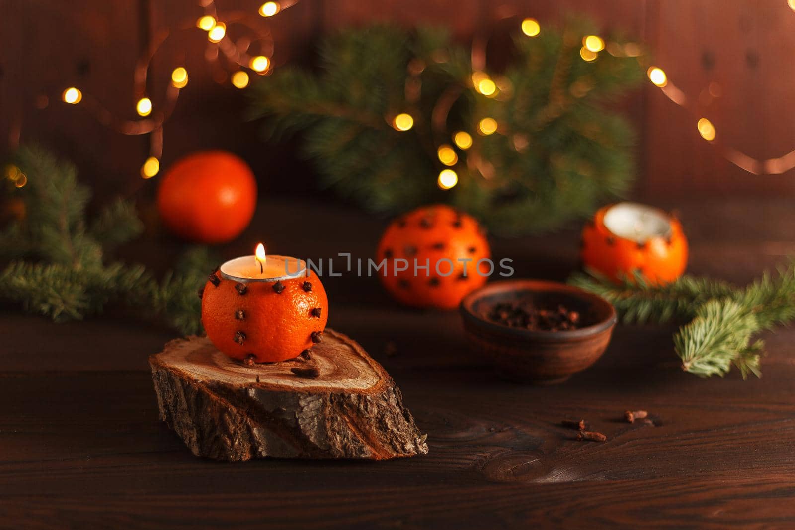 A tangerine candlestick on a wooden stand on a table decorated with fir branches and Christmas lights. Handmade.copy space