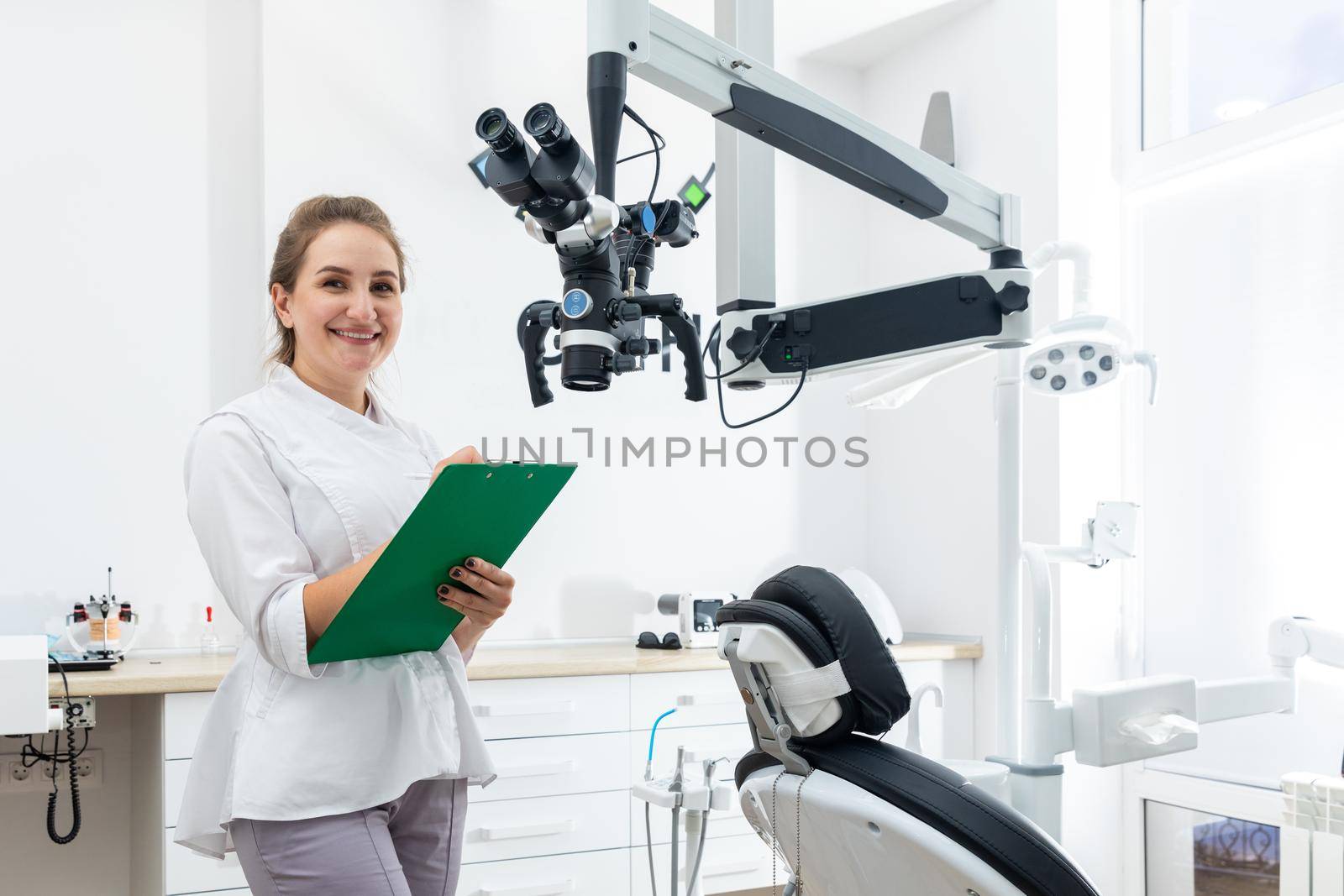 Smiling female dentist holding a clipboard with patient records in hands at dental clinic