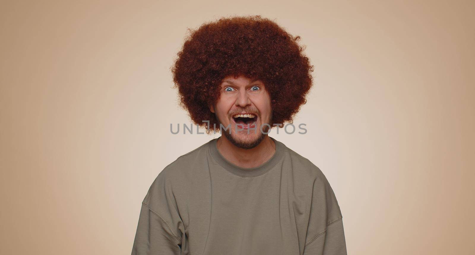 Joyful man with lush hairstyle laughing out loud after hearing ridiculous anecdote, funny joke, feeling carefree amused, positive people lifestyle. Young guy boy isolated on beige studio background