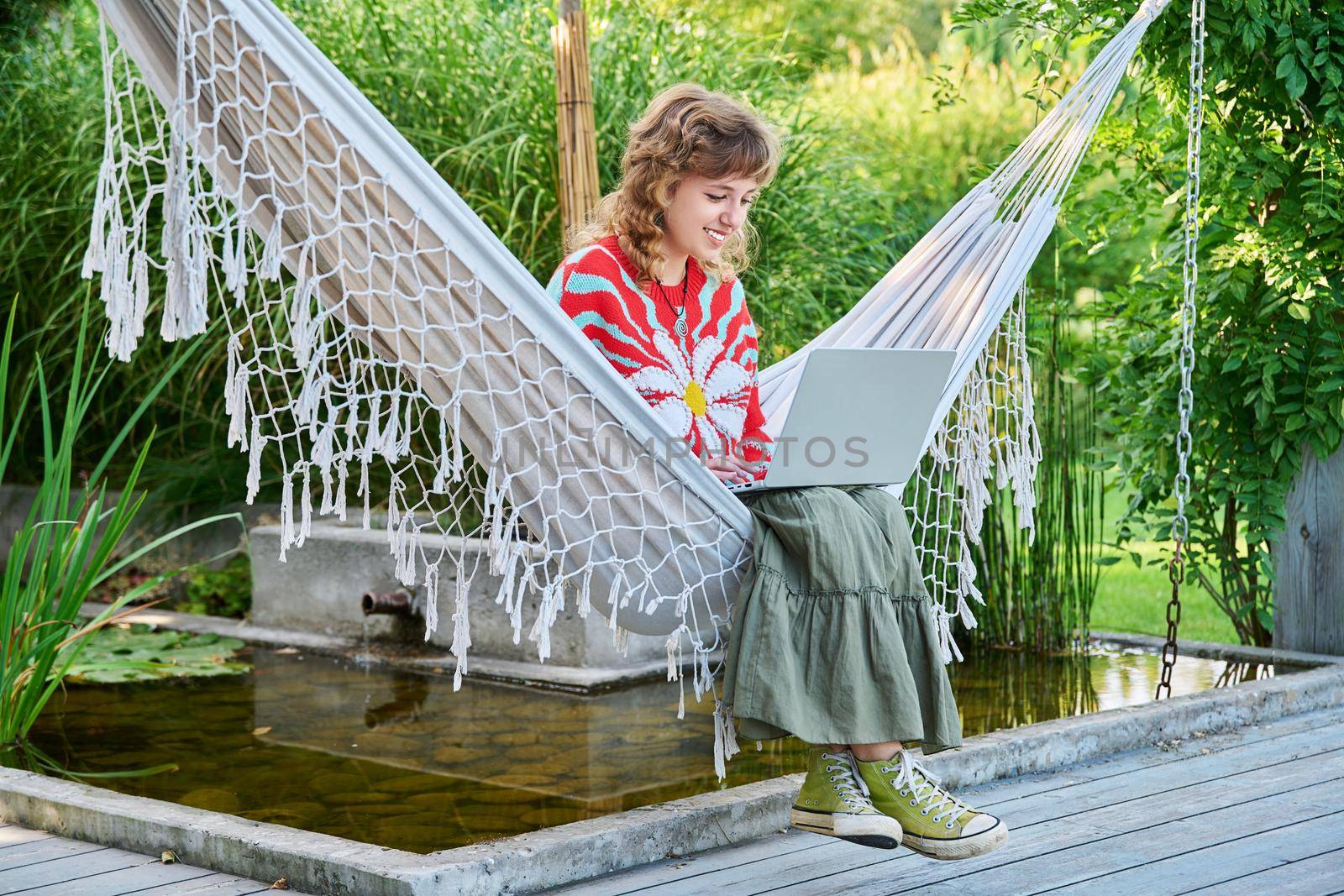 Teenage girl relaxing in hammock using laptop for leisure study. Adolescence, students, high school, technology, lifestyle, youth concept