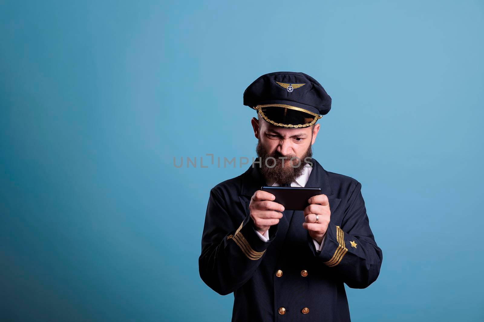 Plane captain in professional uniform playing mobile games on smartphone, holding phone, watching funny video. Airlane captain using aviation simulator on telephone, leisure entertainment