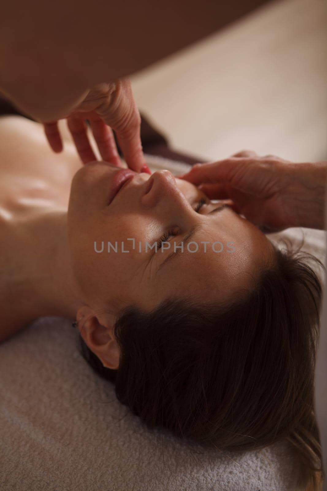 Vertical close up of mature woman enjoying professional anti-aging face massage by spa beautician