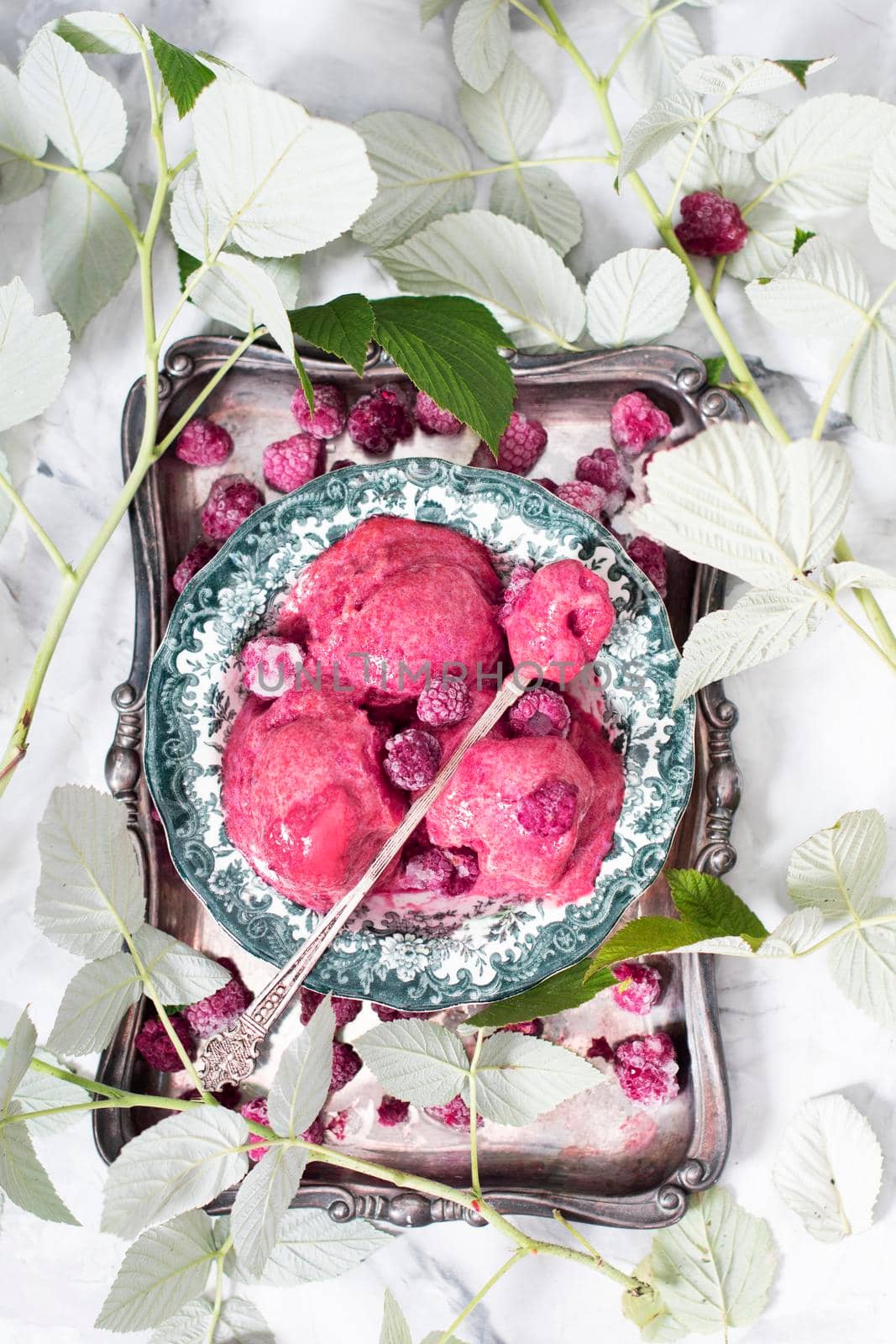 Raspberry purple ice cream sorbet on a silver plate surrounded by green leaves, summer dessert, top view. High quality photo