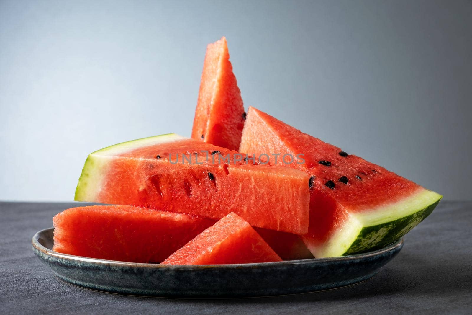 Sliced pieces of ripe sweet watermelon lie on a gray ceramic plate on a gray surface. Selective focus.