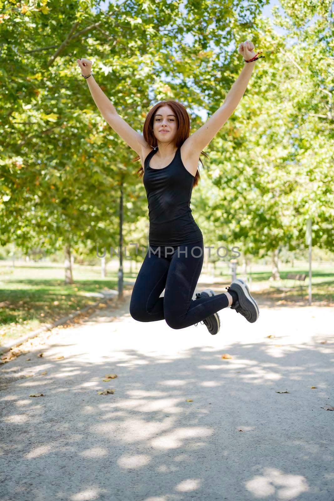 Happy woman jumping on the road while exercising by barcielaphoto