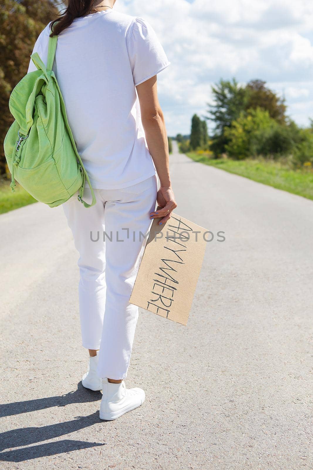 A beautiful girl with a backpack on her shoulder holds a sign with the inscription anywhere. Hitchhiking, adventure